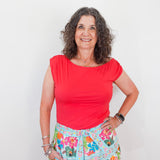 Woman wearing a red top and floral skirt against a white background