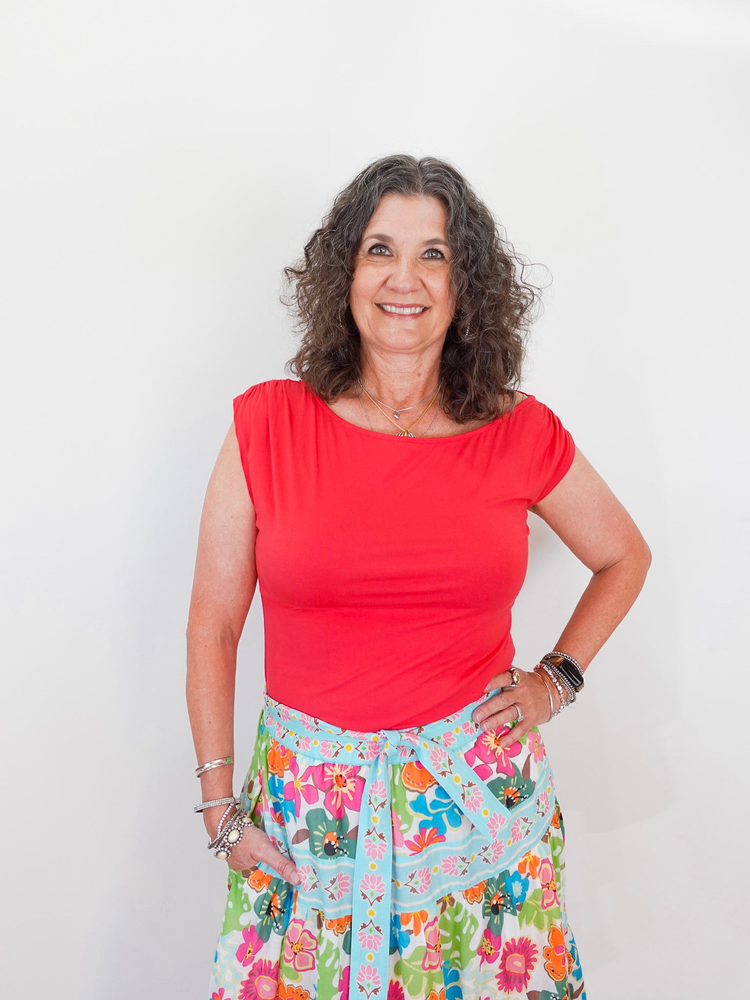 Woman wearing a red top and floral skirt against a white background