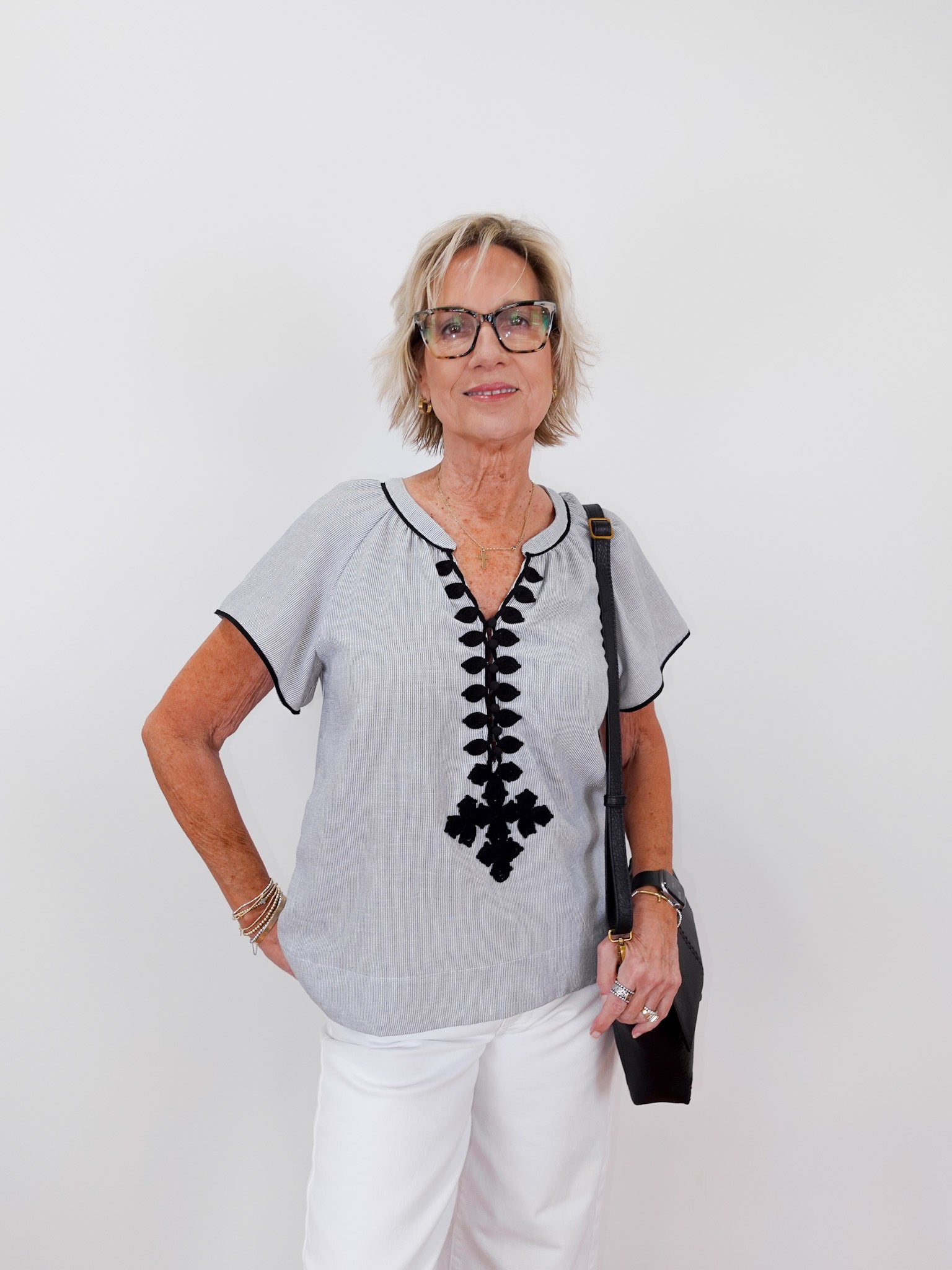 Woman wearing a gray blouse with black lace details and white pants on a plain background