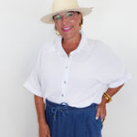 Woman wearing a white shirt, blue pants, and a beige hat against a plain background