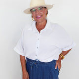 Woman wearing a white shirt, blue pants, and a beige hat against a plain background