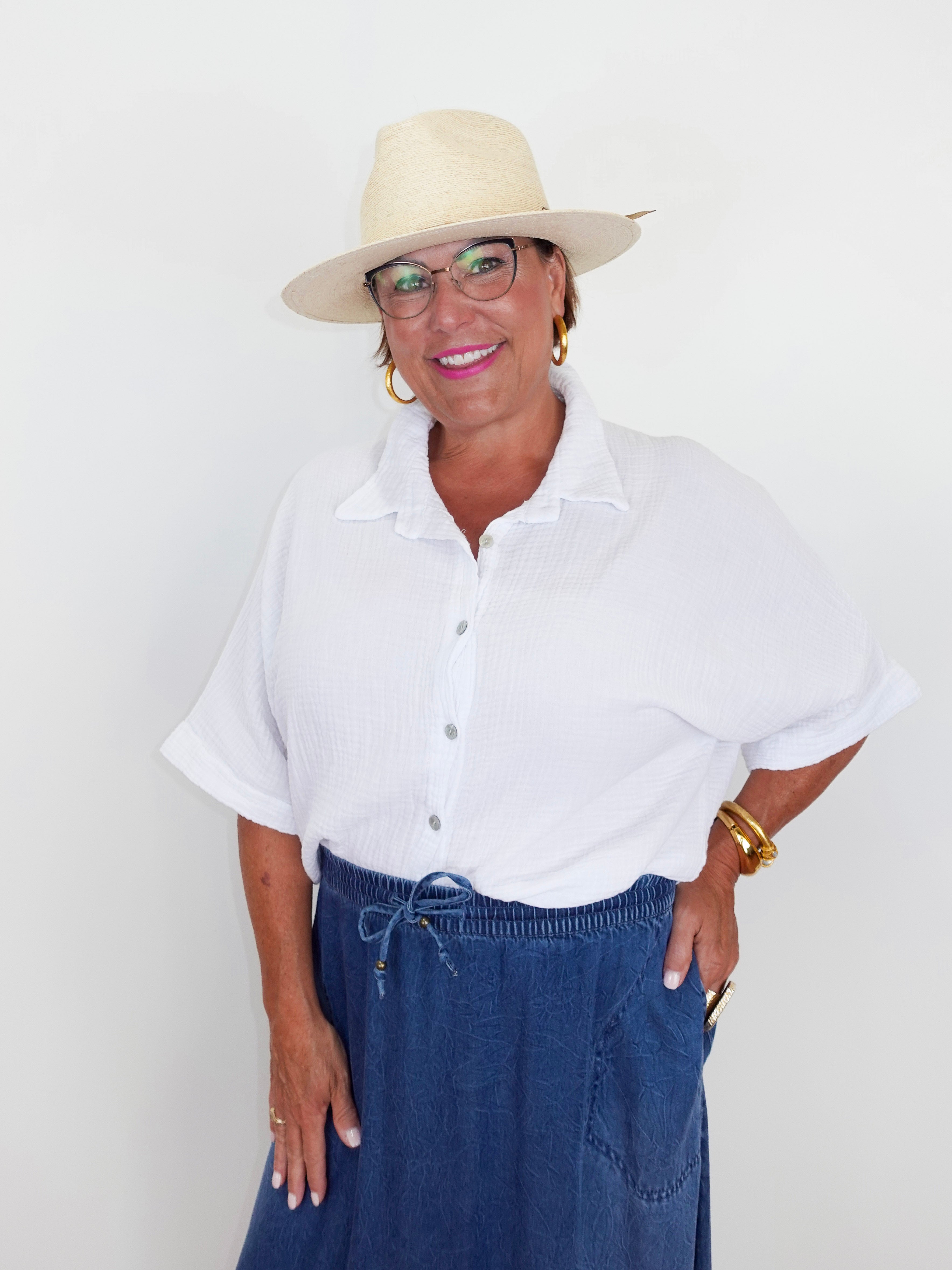 Woman wearing a white shirt, blue pants, and a beige hat against a plain background