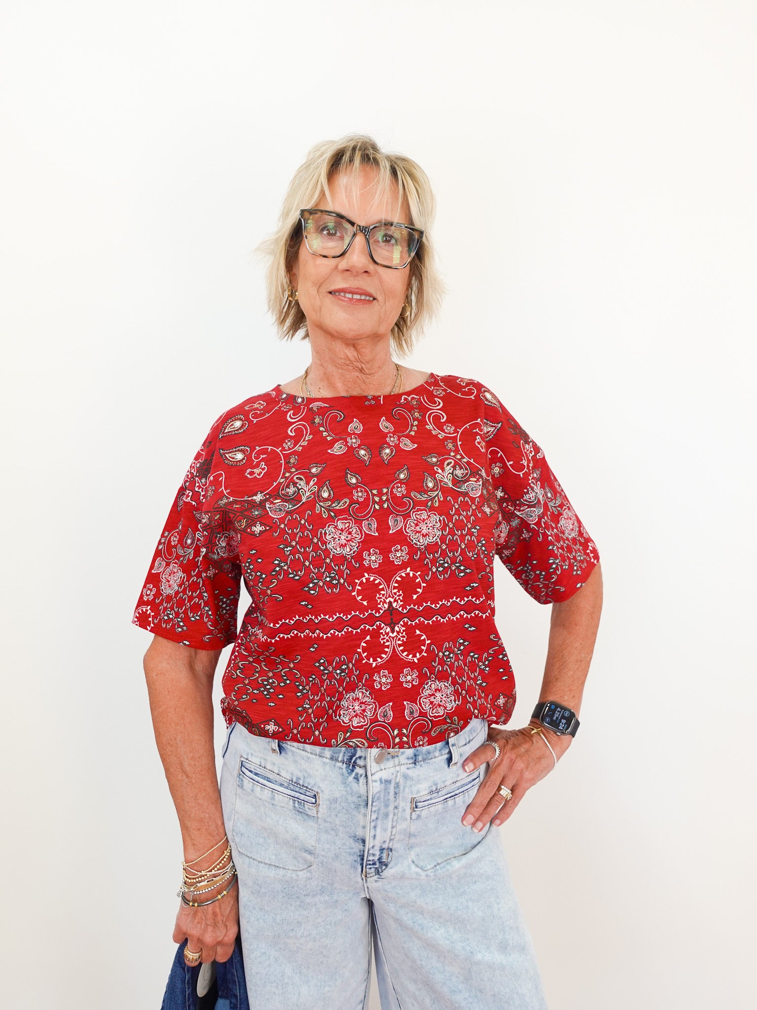 Person wearing a red patterned shirt and light blue jeans against a white background