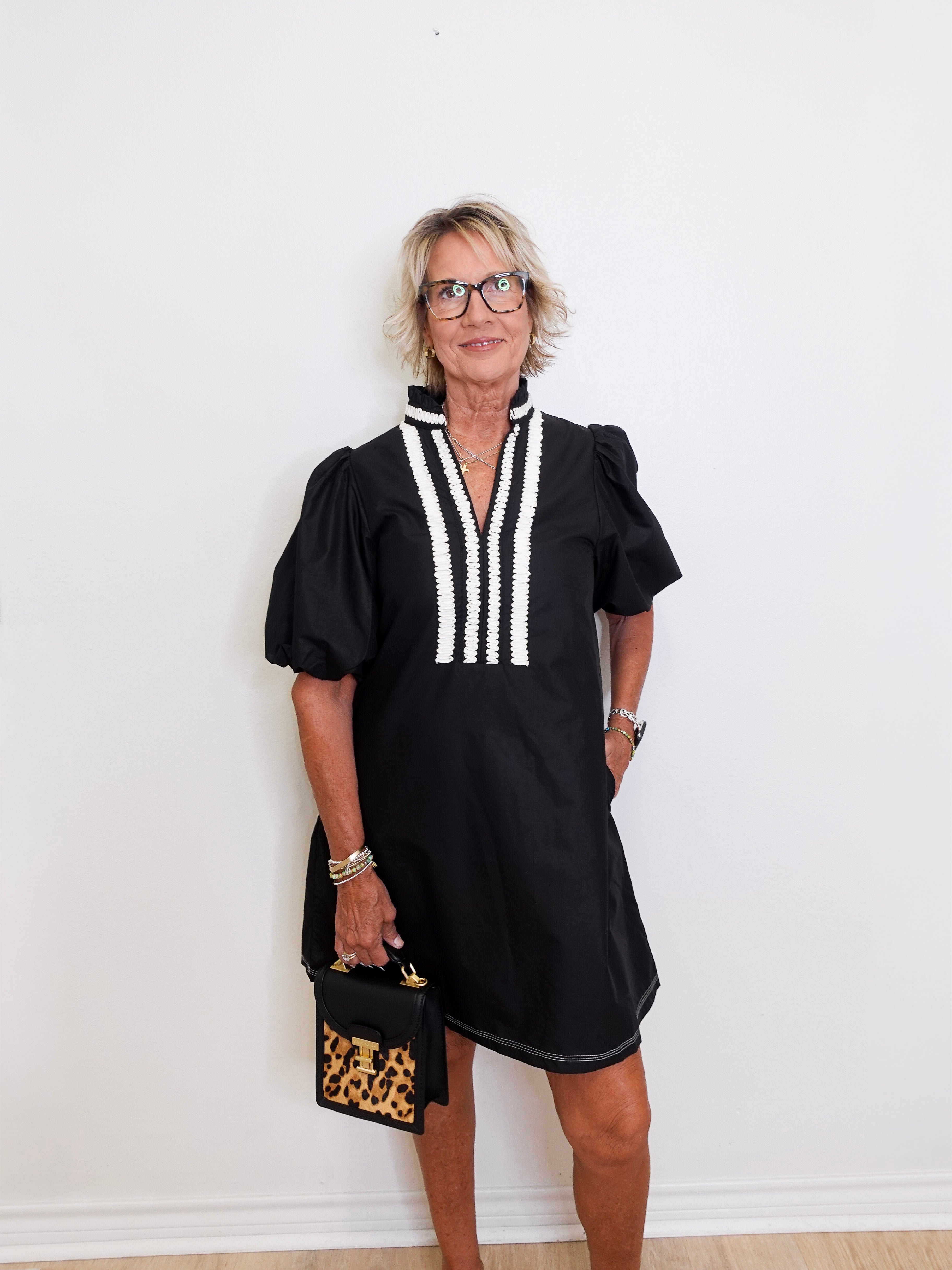 Woman wearing a black dress with white accents against a white wall