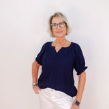 Woman wearing a navy blue top and white pants against a plain background