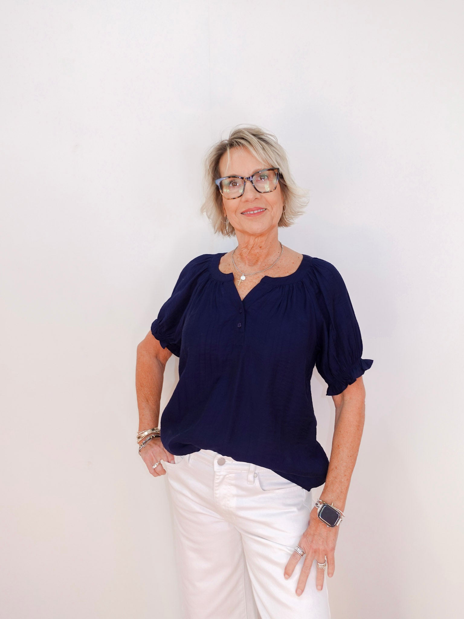 Woman wearing a navy blue top and white pants against a plain background