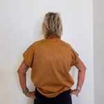 Person wearing a brown suede jacket against a white wall