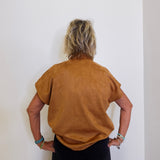 Person wearing a brown suede jacket against a white wall