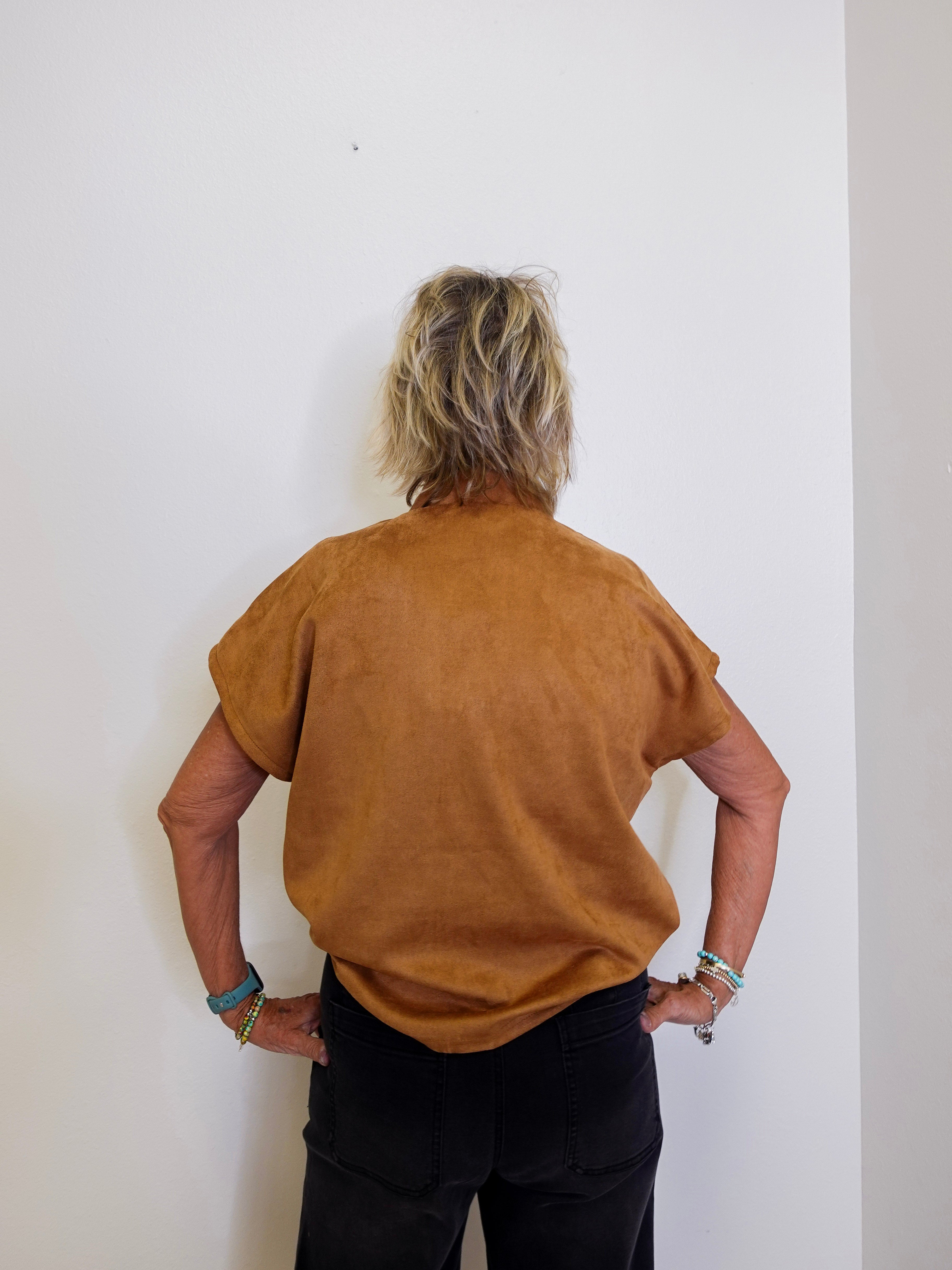 Person wearing a brown suede jacket against a white wall