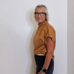 Person wearing a brown top and black pants against a white wall