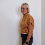 Person wearing a brown top and black pants against a white wall