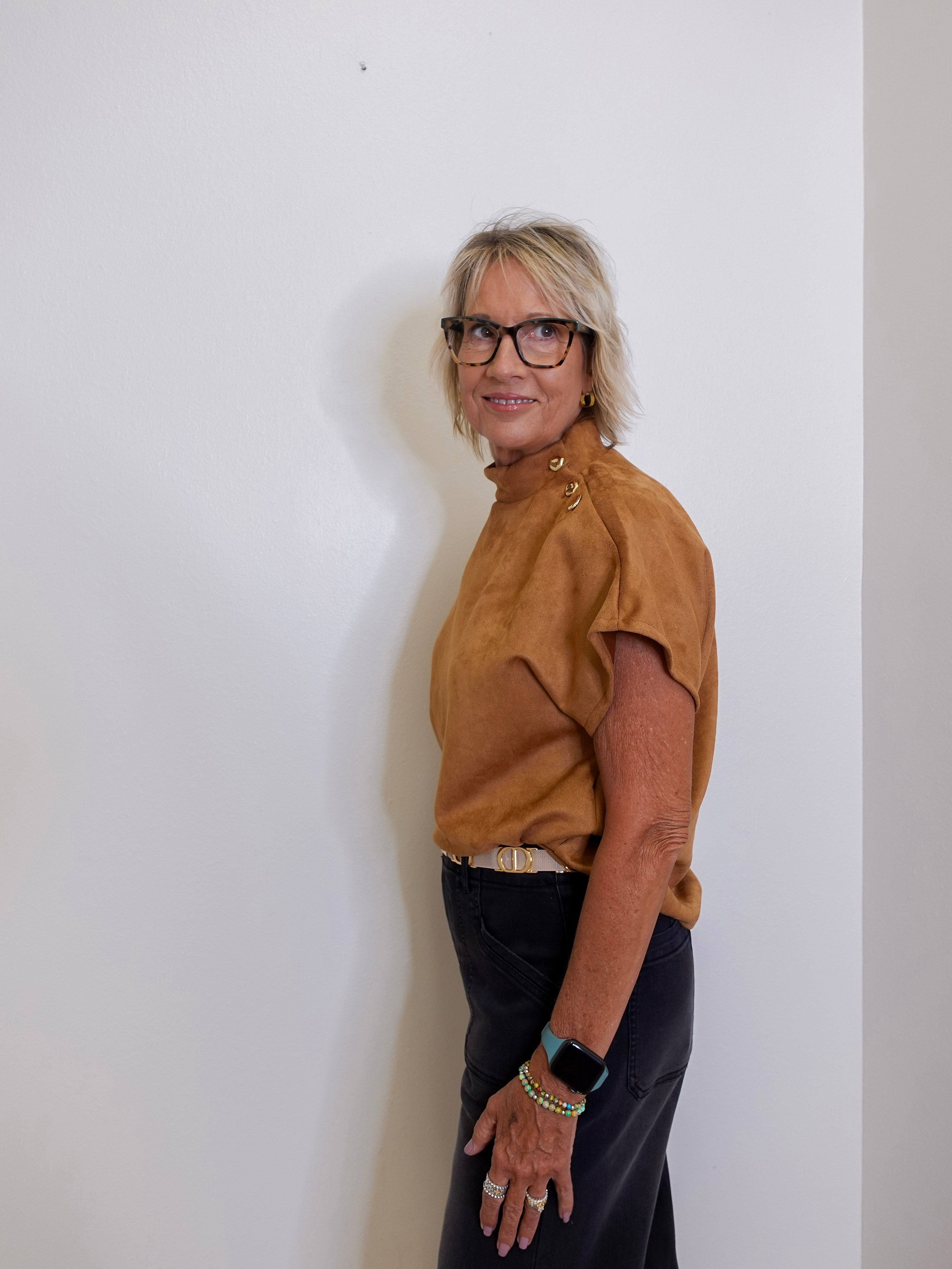 Person wearing a brown top and black pants against a white wall