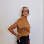 Person wearing a brown turtleneck shirt and black pants against a white background