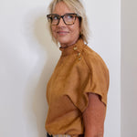 Woman wearing a brown top and glasses against a white wall