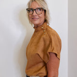 Woman wearing a brown top and glasses against a white wall