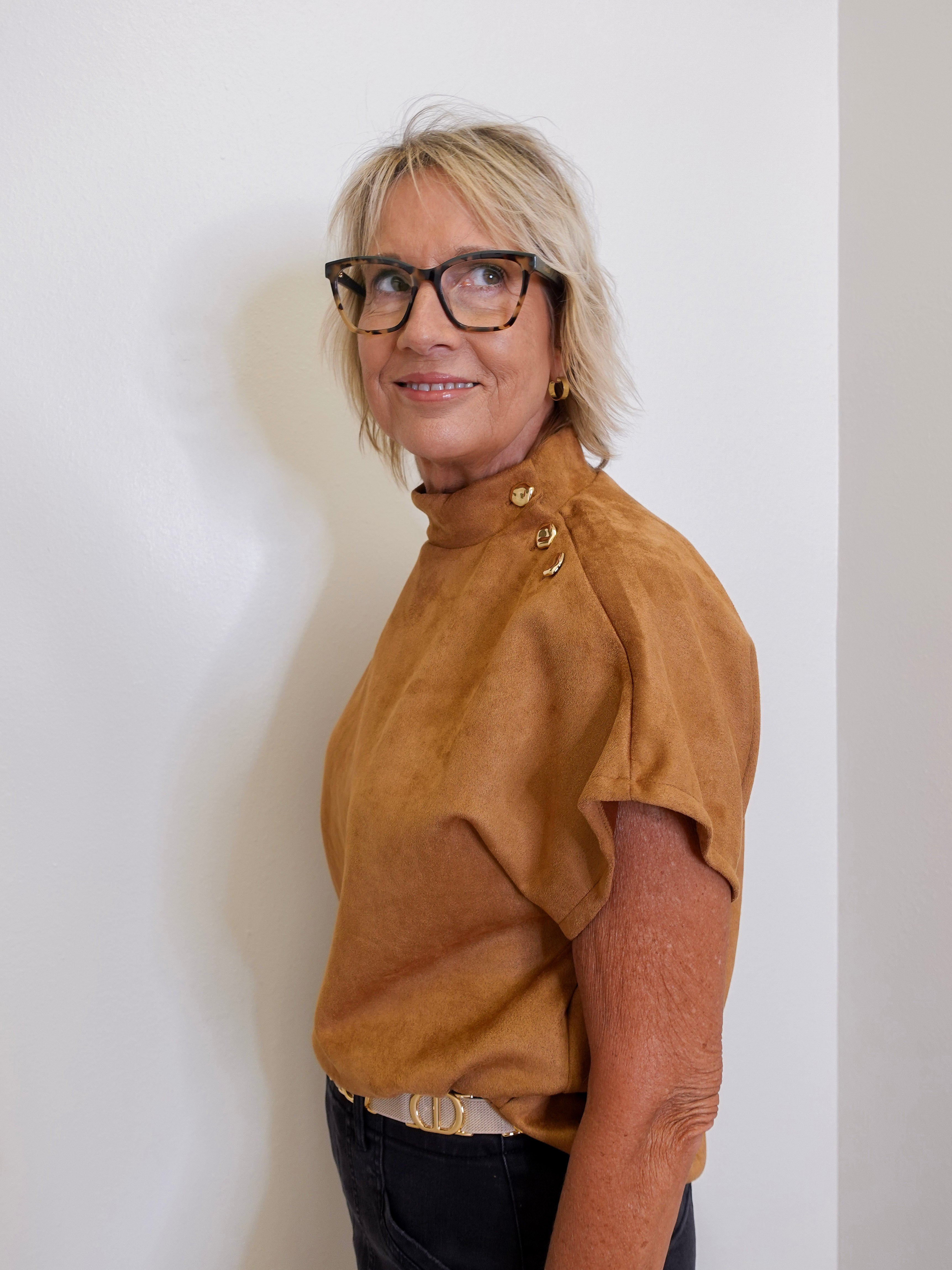 Woman wearing a brown top and glasses against a white wall