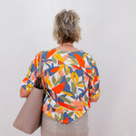 Person wearing a colorful patterned shirt holding a beige bag against a white background