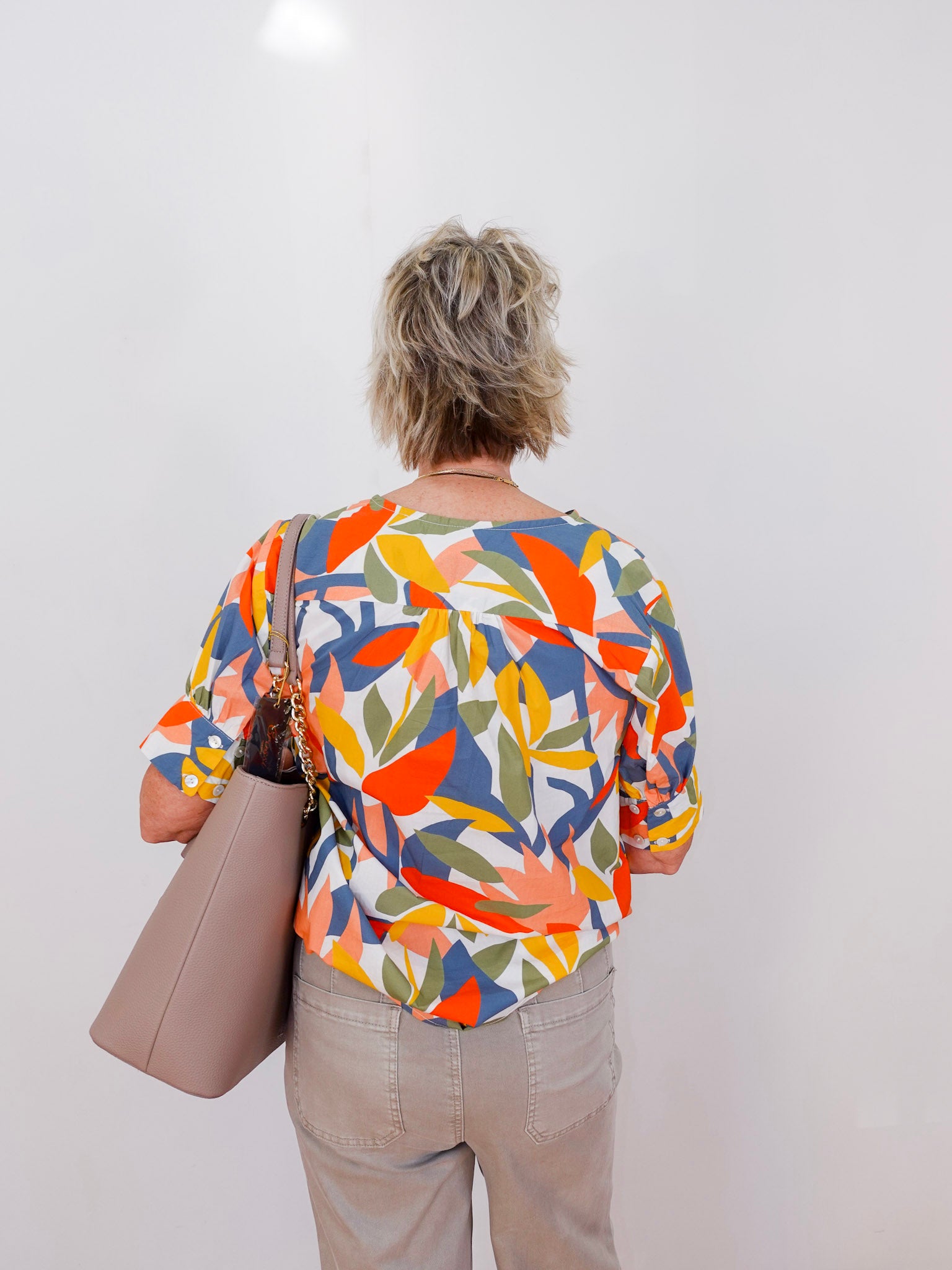 Person wearing a colorful patterned shirt holding a beige bag against a white background