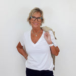 Woman wearing a white shirt and dark pants against a plain background