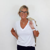 Woman wearing a white shirt and dark pants against a plain background