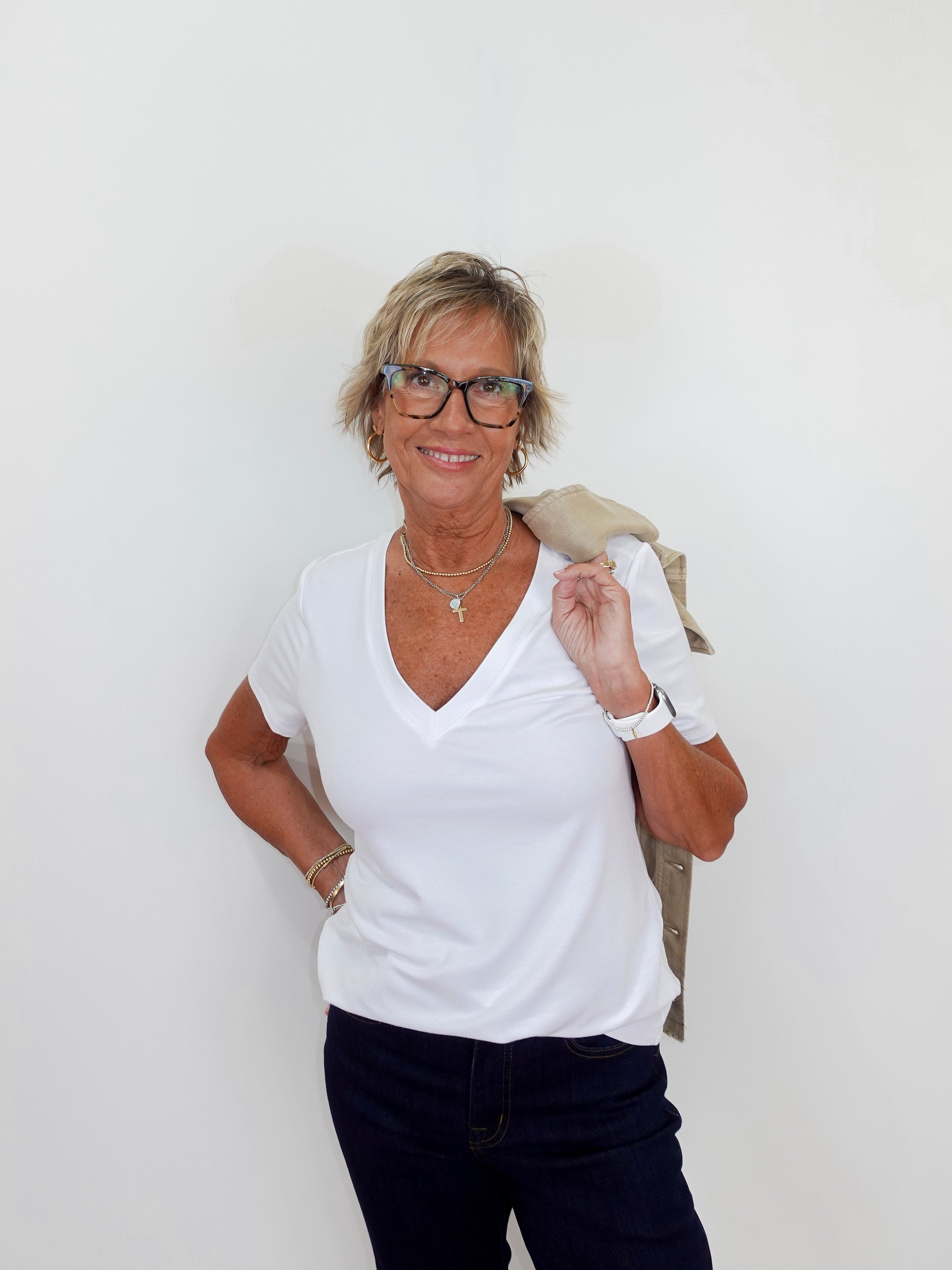 Woman wearing a white shirt and dark pants against a plain background