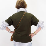 A person shown from the back wearing an olive green short-sleeve cardigan over a white and navy striped shirt, paired with light blue jeans and a brown leather crossbody bag, against a plain white background.