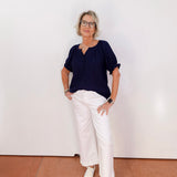 Person wearing a navy top and white pants against a plain background