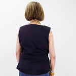 Person wearing a black sleeveless top and blue jeans against a white background