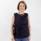 Woman wearing a black sleeveless top with a knot detail and blue pants against a white background