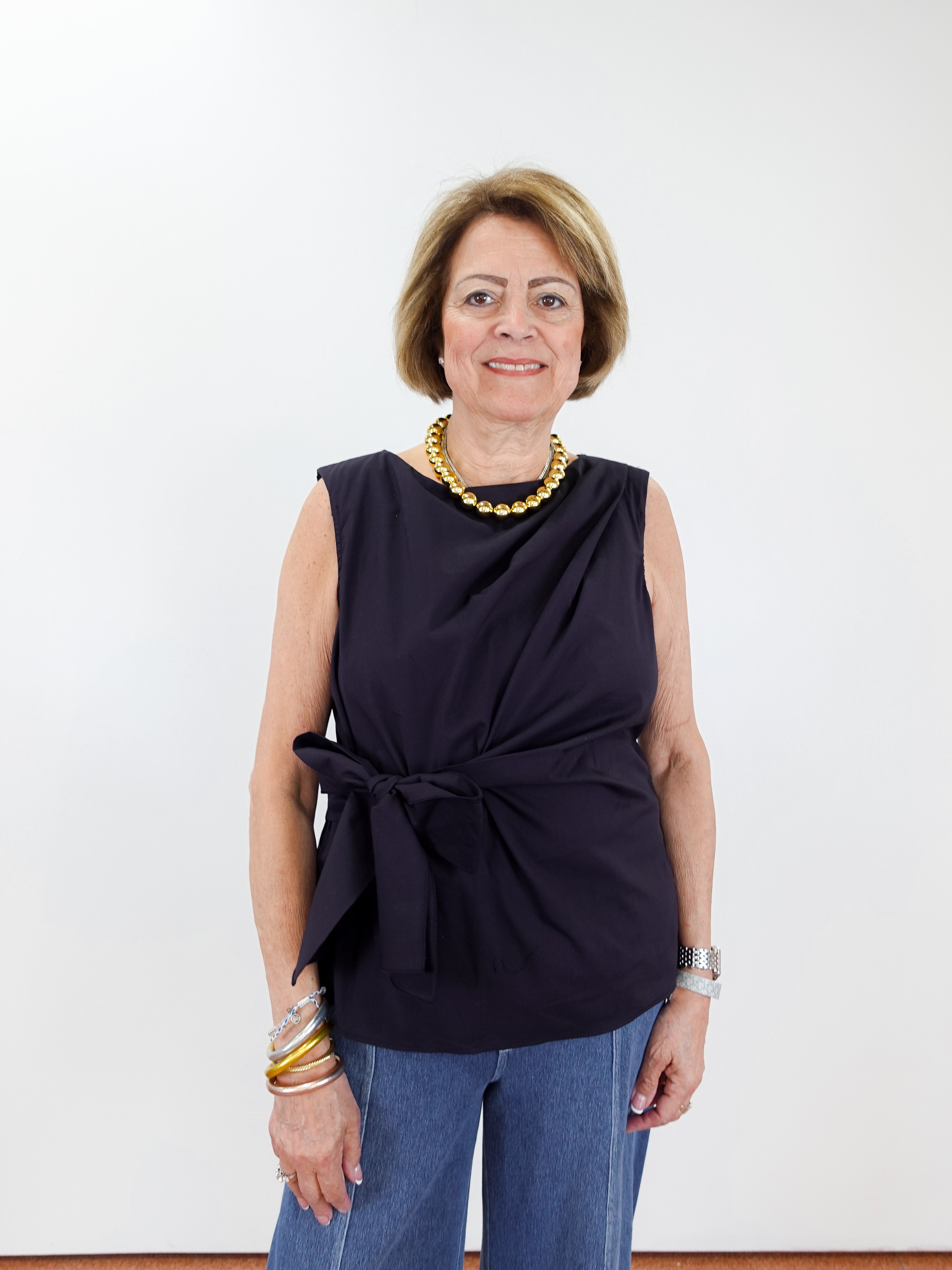 Woman wearing a black sleeveless top with a knot detail and blue pants against a white background