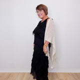 Woman wearing a black dress with ruffles and a beige cardigan against a white wall.