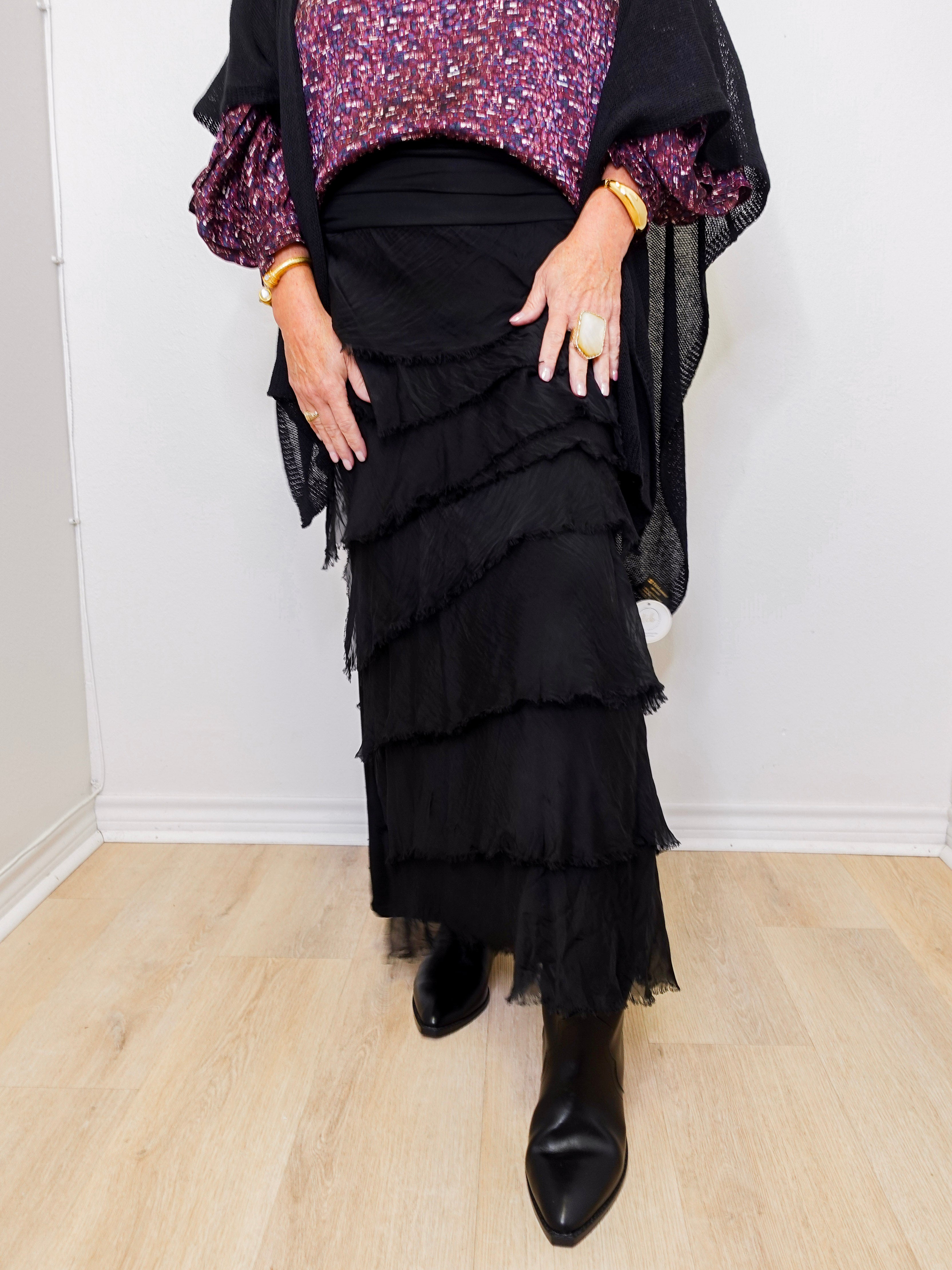 Person wearing a black ruffled skirt with a purple top and black shoes on a light wood floor.