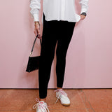 Person wearing a white shirt, black leggings, and white sneakers against a pink wall.
