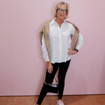 Person wearing a white shirt, black pants, and white sneakers against a pink wall.