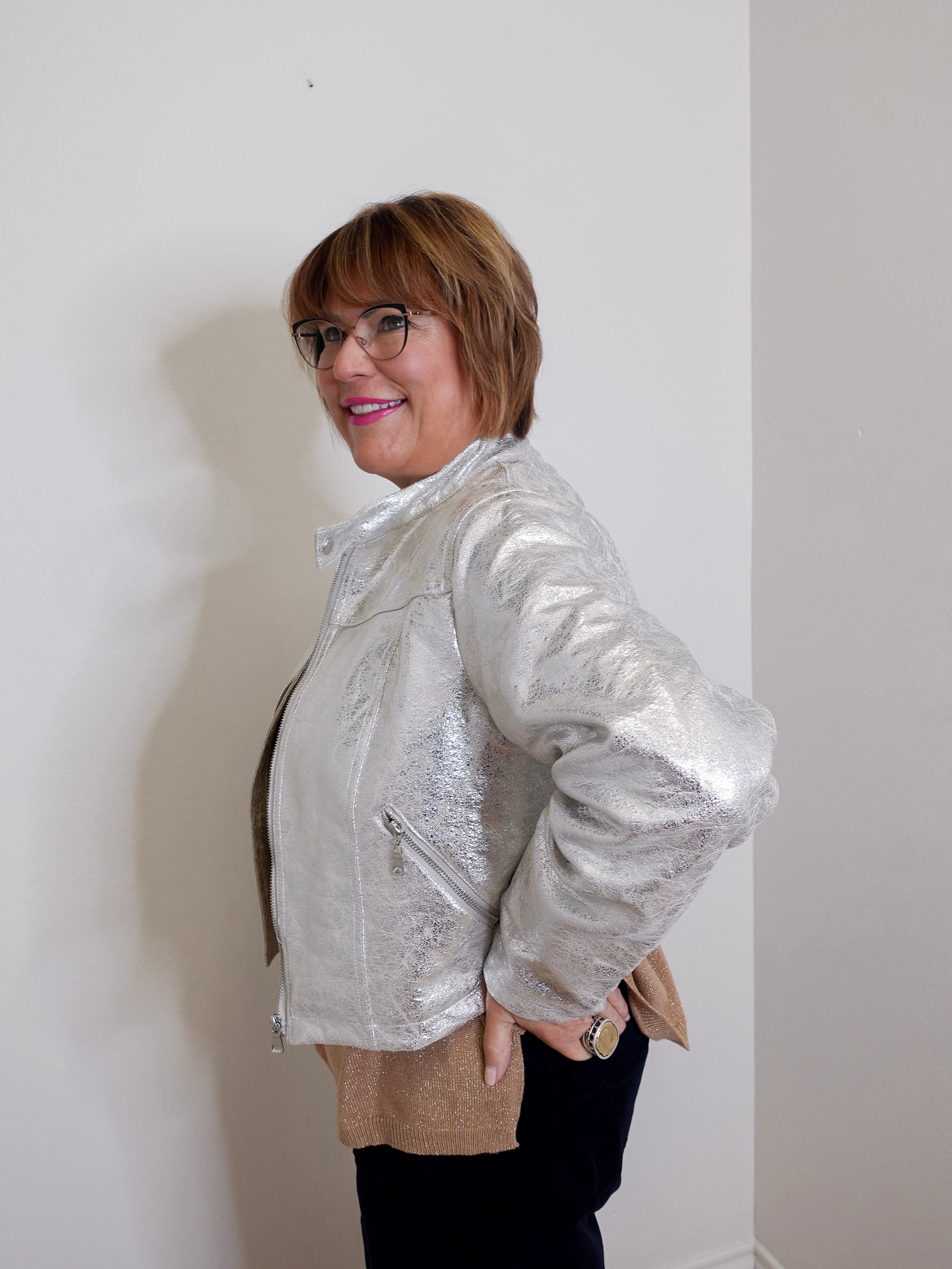 Person wearing a silver jacket against a white wall