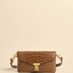 Brown crocodile-patterned handbag with gold hardware on a beige background