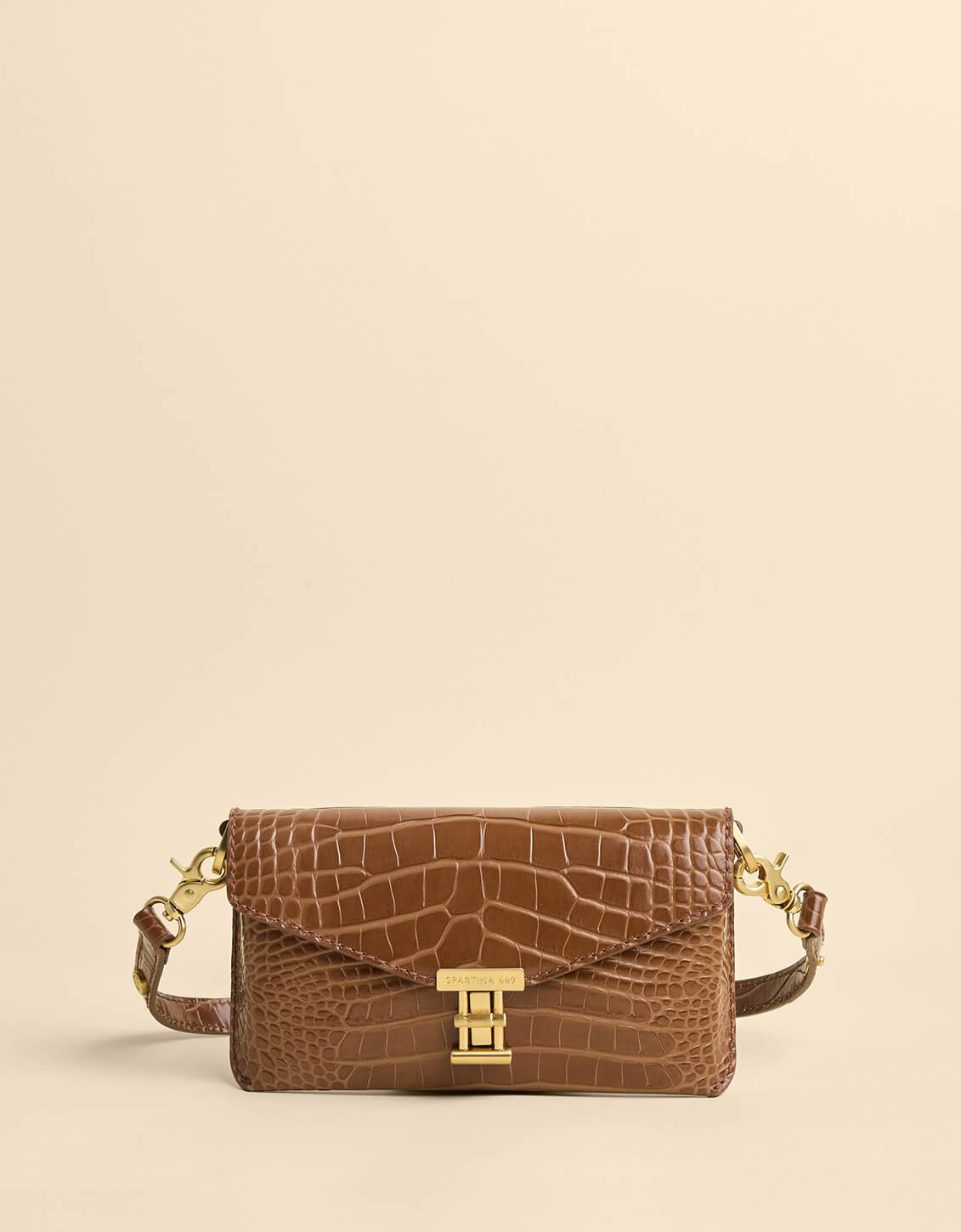 Brown crocodile-patterned handbag with gold hardware on a beige background