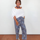 Woman wearing a white blouse and blue patterned pants against a white wall.