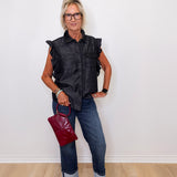 Woman wearing a black sleeveless shirt, blue jeans, and holding a red handbag against a white background