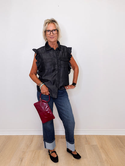 Woman wearing a black sleeveless shirt, blue jeans, and holding a red handbag against a white background