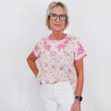 Woman wearing a pink floral blouse and white pants against a plain background