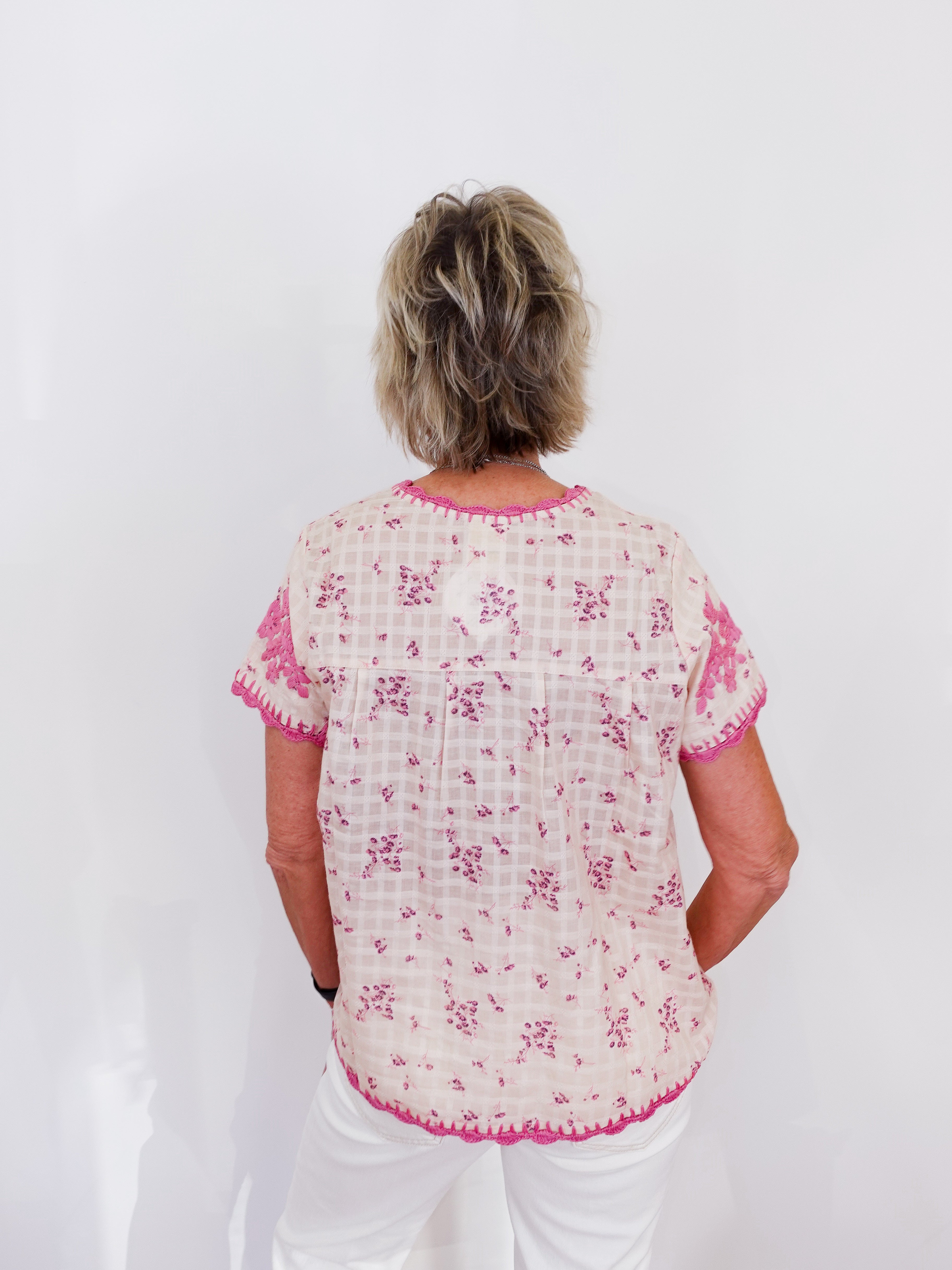 Woman wearing a white blouse with pink floral patterns on a white background