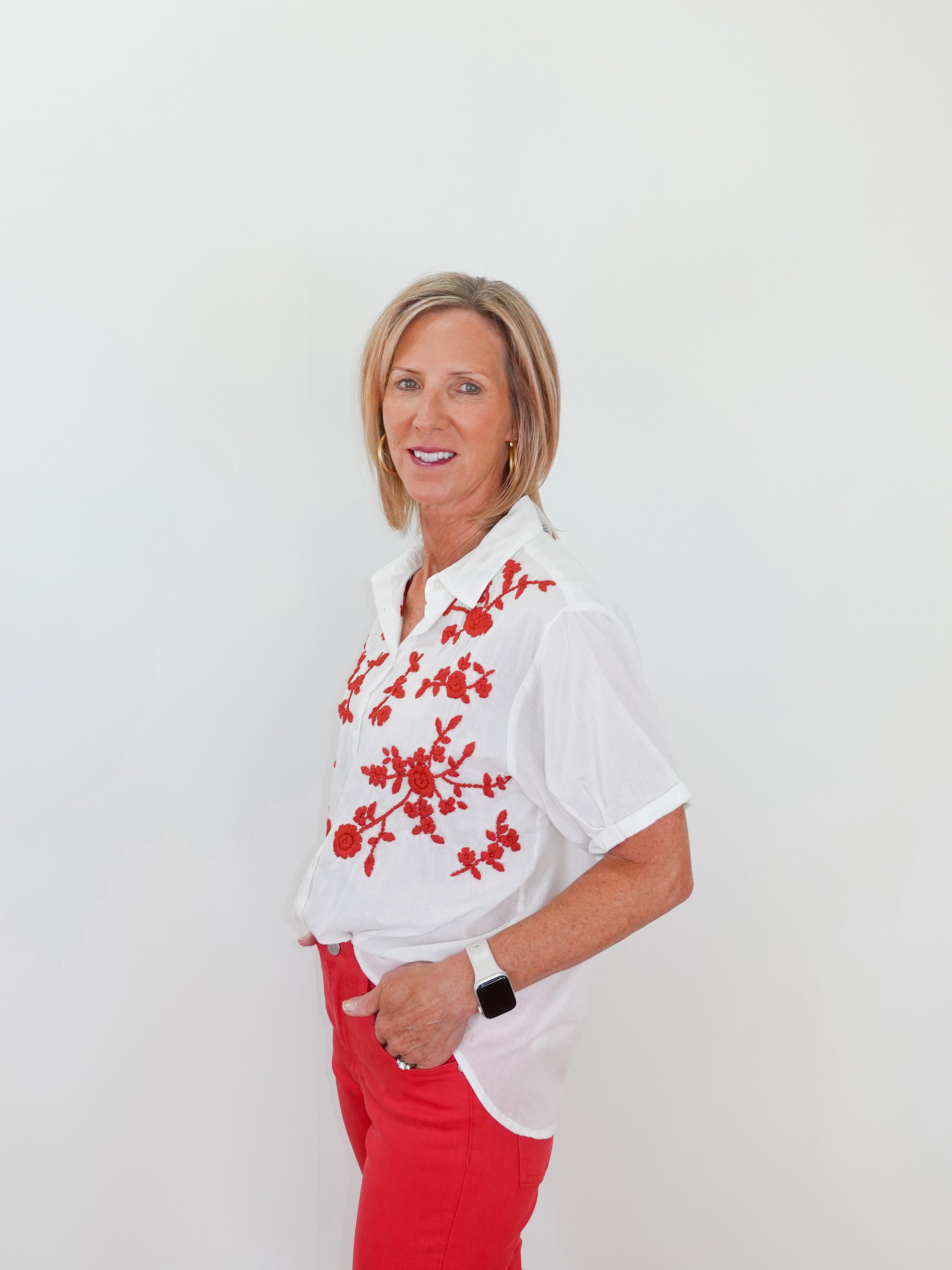 Woman wearing a white blouse with red floral patterns and red pants on a white background