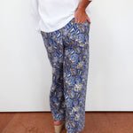 Person wearing blue paisley pants with a white shirt against a white wall.