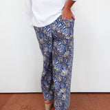 Person wearing blue paisley pants with a white shirt against a white wall.