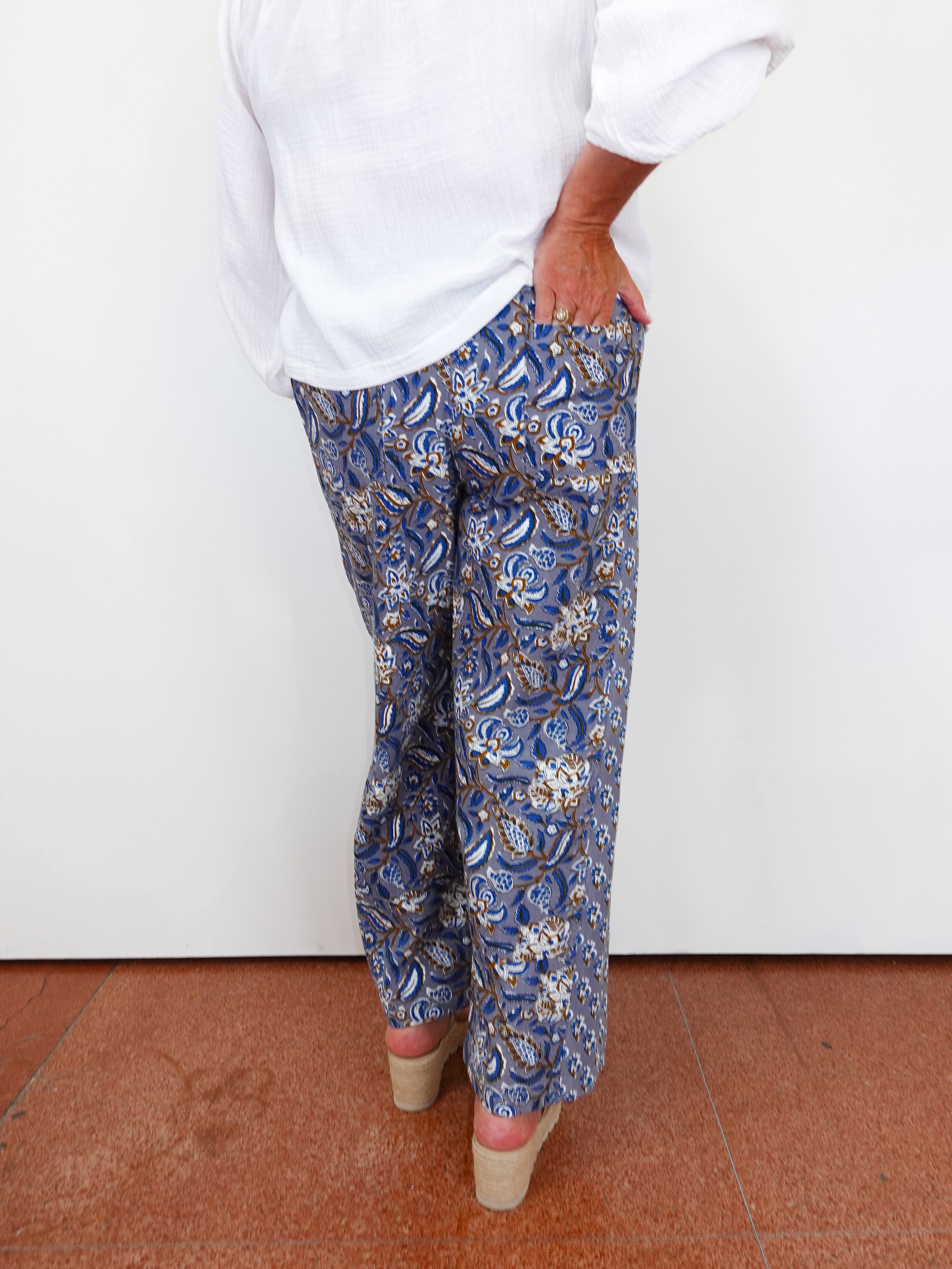 Person wearing blue paisley pants with a white shirt against a white wall.
