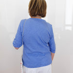 Person wearing a blue shirt and white pants standing against a white wall.