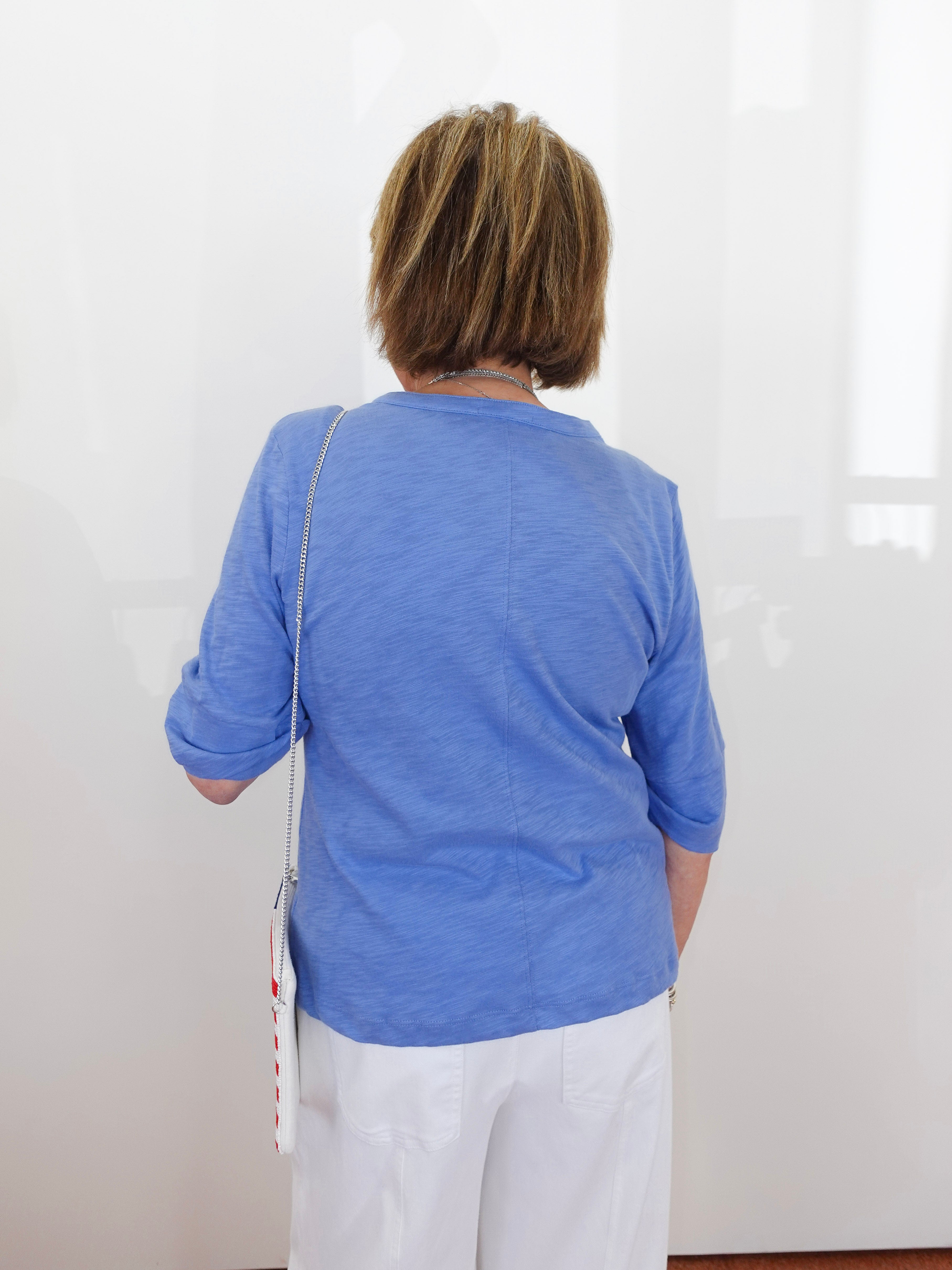 Person wearing a blue shirt and white pants standing against a white wall.