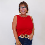 Woman wearing a red sleeveless top and blue jeans against a white background