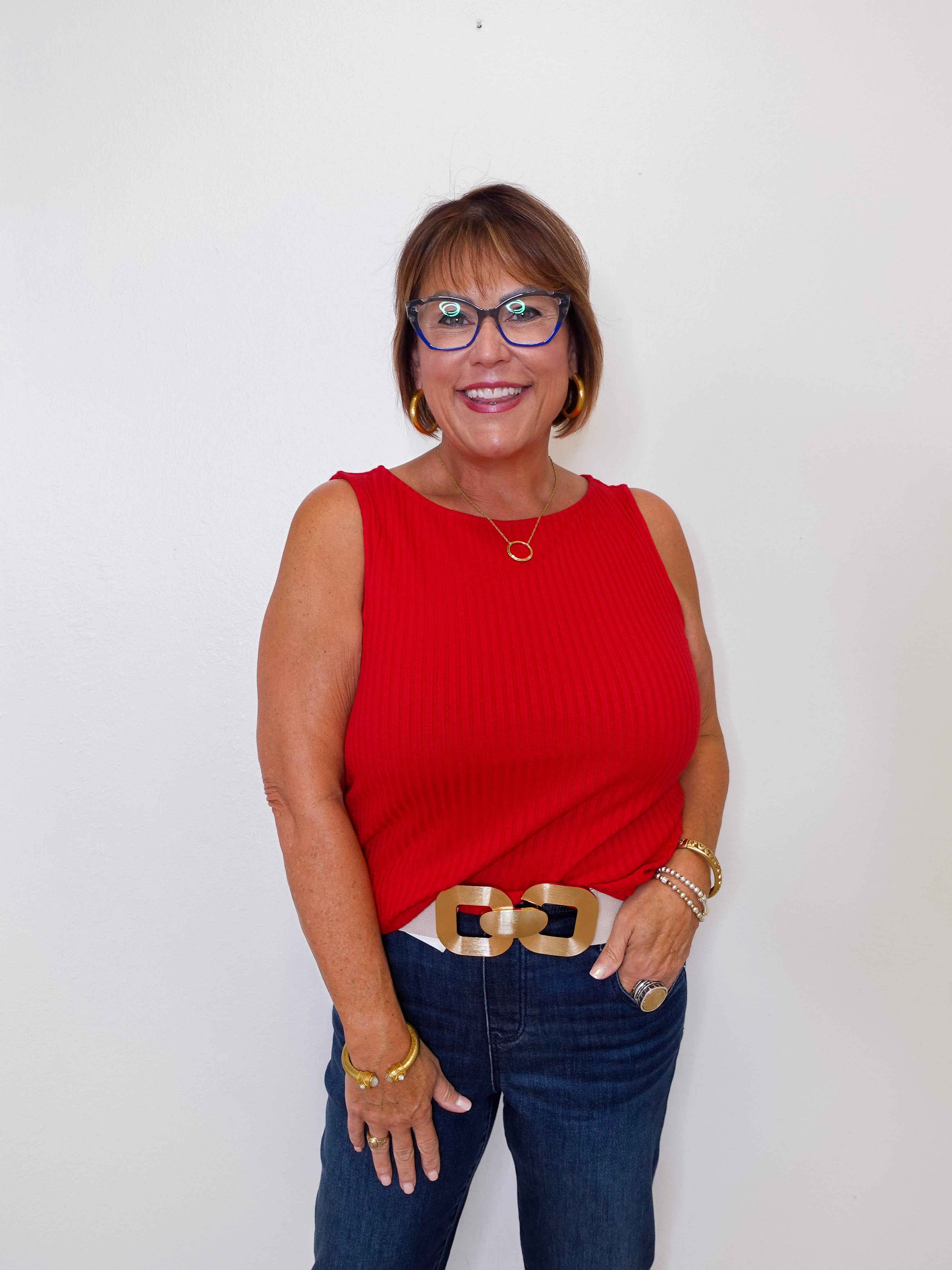 Woman wearing a red sleeveless top and blue jeans against a white background
